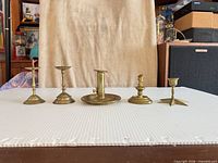 Front view of all five brass candlesticks aligned on surface