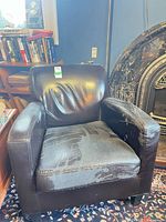 Front view of black faux leather armchair showing overall design and wear