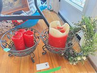 Overview of two metal candle holders with red candles and faux floral wreath