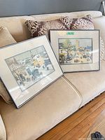 Both framed village scene artworks on sofa