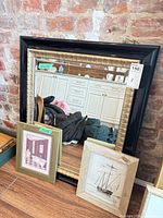 Group shot of mirror with black and gold frame and two smaller framed prints leaning against it
