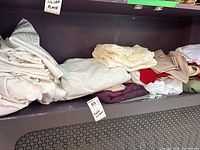 Stack of folded white, cream and coloured tablecloths on shelf