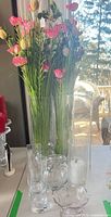 Group shot showing tall cylinder with faux flowers and smaller glass vases on table