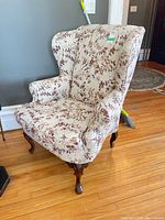 Front view of floral wing back armchair with curved wooden legs