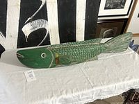 Left side view of green wooden fish puppet on table showing full length and scale pattern