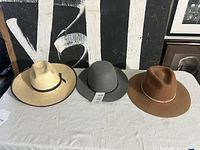 Three hats laid out: palm leaf, grey felt, brown felt