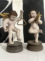Full view of both putti figurines showing instruments and bases
