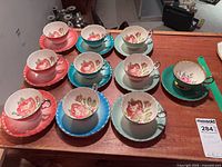 Ten colored Aynsley teacups on matching saucers displayed on table