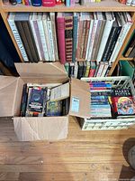 Cardboard box of assorted paperbacks and plastic crate of additional books with visible Harry Potter hardcover