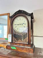 Front view of figured veneer mantel clock showing dial, glass door and carved crest