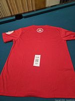 Back view of red T-shirt showing circular crown logo and sleeve patch