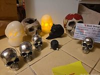 Group shot of all skull items including LED candles lit, silver skull card holders, ceramic skull, wood devil head, novelty skull ball