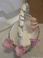 Angled view of porcelain basket showing bunny figure, pink flowers, vine handle