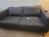 Front view of charcoal fabric loveseat showing seat and back cushions, wooden legs