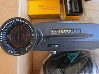 Front view of Kodak Carousel 860H projector with attached Ektanar lens, lens cap visible, part of remote and cords seen