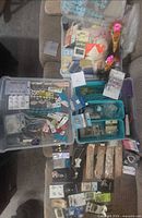 Overview of two open storage tubs filled with packaged beads, findings, trims and tools laid out on couch