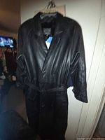 Full view of black leather trench coat on hanger showing length and overall condition
