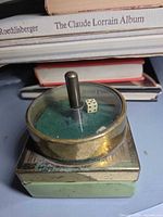 Brass and glass dice spinner atop metal box, dice visible