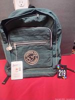 Front view of dark green Northern Duck backpack showing logo patch, front zipper pocket and attached hang tags