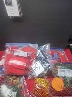 Overview showing several labeled Ziplock bags containing red fabric items, gold and red bead strands, and artificial floral picks
