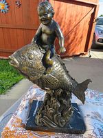 Front view of bronze boy on fish statue showing full form and marble base