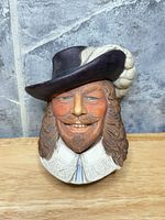 Front view of the painted plaster cavalier wall head showing facial features, hat, plume, and collar