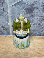 Front view of porcelain figurine trinket box showing green bodice and blue floral skirt