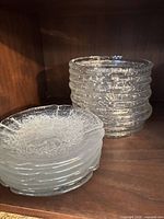 Two stacks of clear pressed glass plates showing quantity difference and overall condition