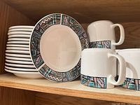 Stack of saucers next to mugs showing geometric band design