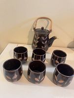 Teapot front with rattan handle and six cups displayed