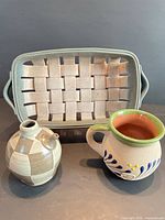 Three stoneware pieces: woven tray, spouted vessel, painted mug