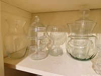 Four glass pieces: flared vase, three-section jar with lid, hourglass vase, bulbous jar with lid