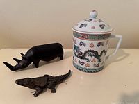 Porcelain mug, wood rhino, metal crocodile grouped