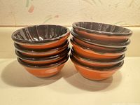 Stacked view of nine orange-exterior, dark-interior stoneware bowls