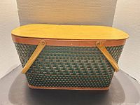 Front view of oval green woven basket with hinged wood lid and swing handles