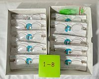 Open box showing two stacks of packaged rimless eyeglass frames and green screwdriver kit