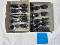 Two open boxes showing eleven sleeved black sunglasses