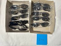 Two shallow cartons with 13 black sunglasses pairs, mostly bagged