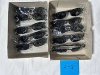 Two cardboard trays holding ten individually wrapped black sunglasses