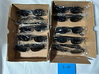 Two open cardboard trays holding ten sealed black sunglasses
