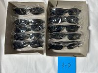 Two boxes holding ten sealed pairs of black sunglasses