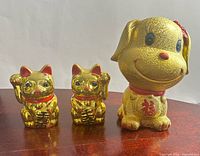 Front view of two gold fortune cat piggy banks and gold glitter dog piggy bank