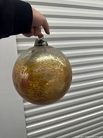 Large gold glass ornament held to show scale and finish