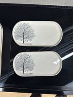 Top view of two small oblong serving plates showing tree motif and gold rim