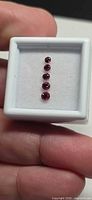 Six graduated round rubies in gem box held by fingers