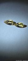 Two pear-cut golden yellow heliodor gemstones side by side on neutral background