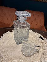 Decanter with stopper and creamer displayed on lace mat