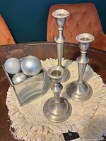 Three pewter candlesticks, glass cube candle holder with silver balls on lace mat