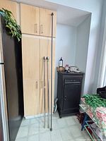 Four rod sections forming two telescoping curtain rods with ball finials leaning against cabinetry