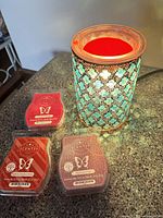 Turquoise mosaic Scentsy warmer lit with red wax and three Scentsy wax bars